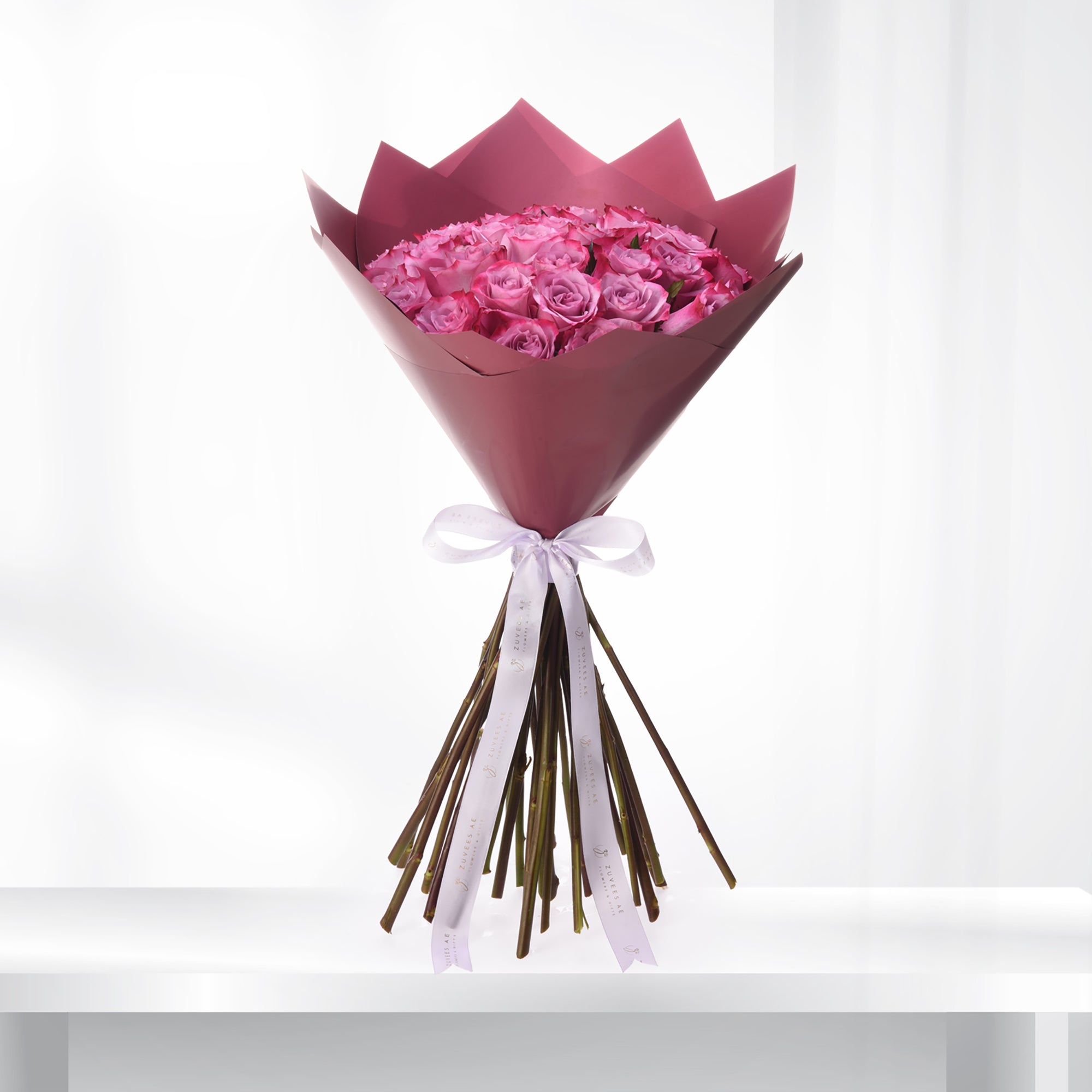 Vibrant pink roses in burgundy paper, elegantly tied with white ribbon.