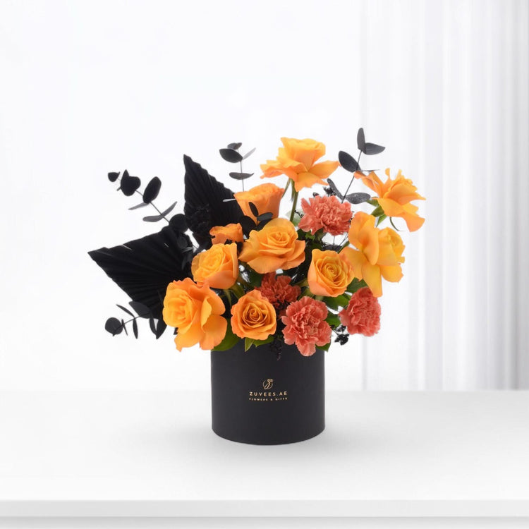 Vibrant orange roses and carnations contrast elegantly with black foliage in a sleek black box.