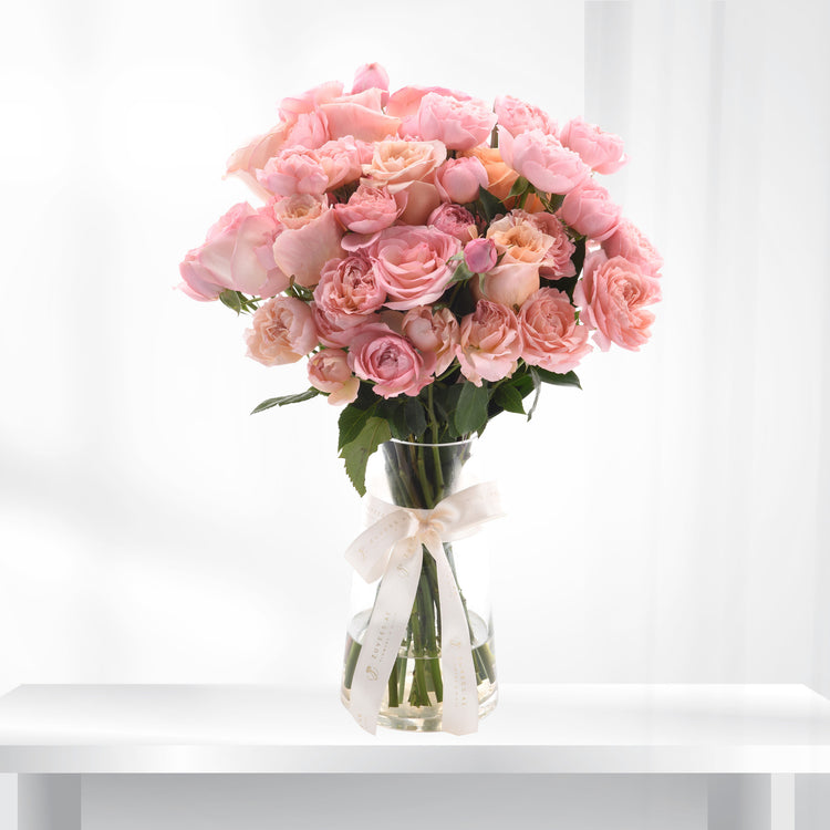 Soft pink roses in clear vase, elegantly tied with cream ribbon.