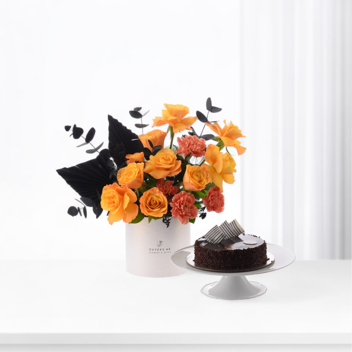Vibrant orange roses and coral carnations contrasted with black foliage, beside chocolate cake.