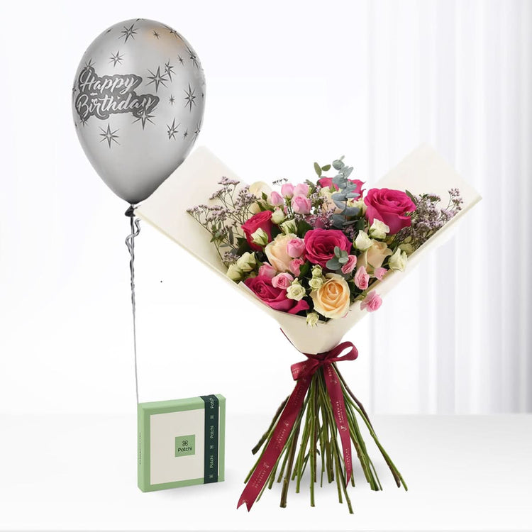 Silver "Happy Birthday" balloon floats beside vibrant rose bouquet with burgundy ribbon and green gift box.