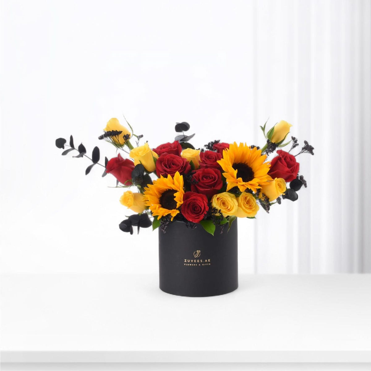 Vibrant red roses and sunflowers in sleek black vase with gold branding.