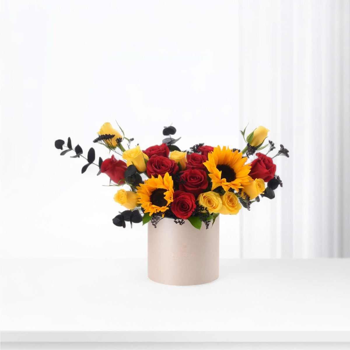 Vibrant red and yellow roses with sunflowers in beige cylindrical vase.