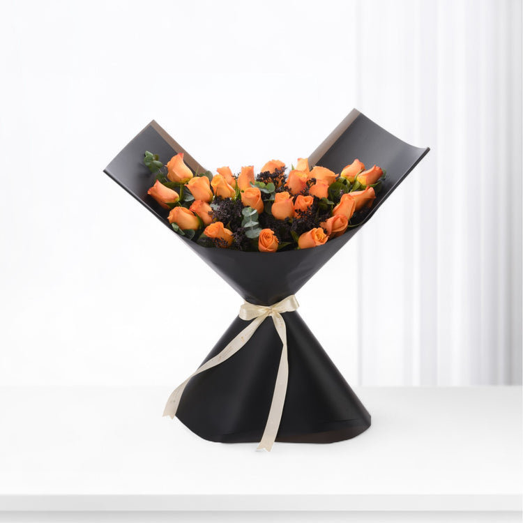 Vibrant orange roses in sleek black paper, accented with cream ribbon and dark foliage.