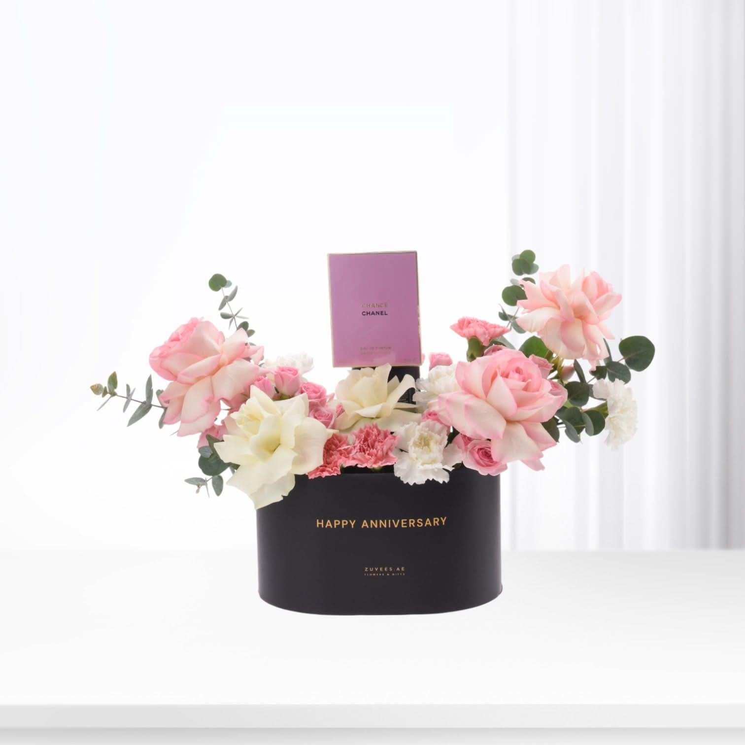 Elegant black anniversary box with pink roses, white blooms, and Chanel perfume.