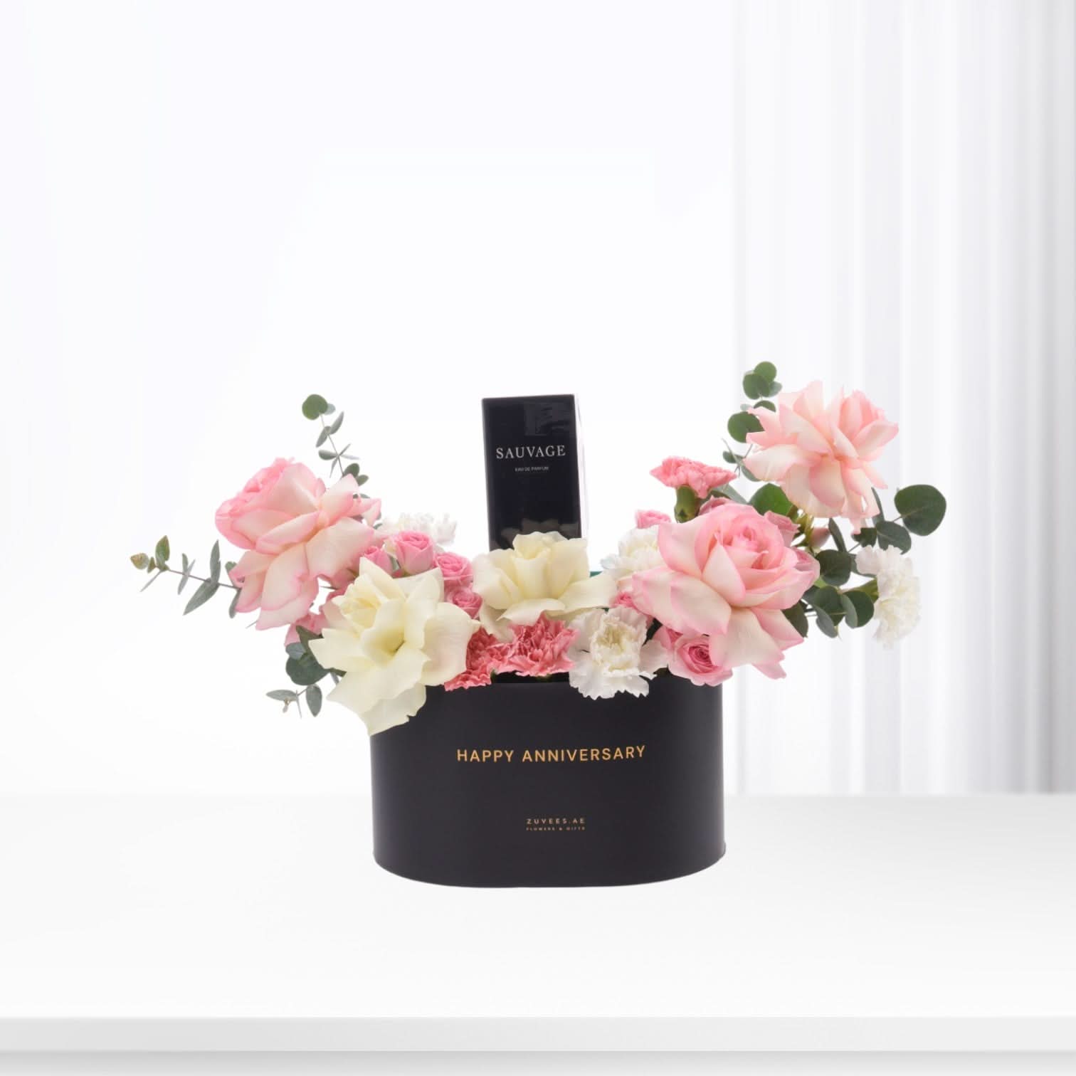 Black box with "Happy Anniversary" holds pink roses, white blooms, and Sauvage perfume.