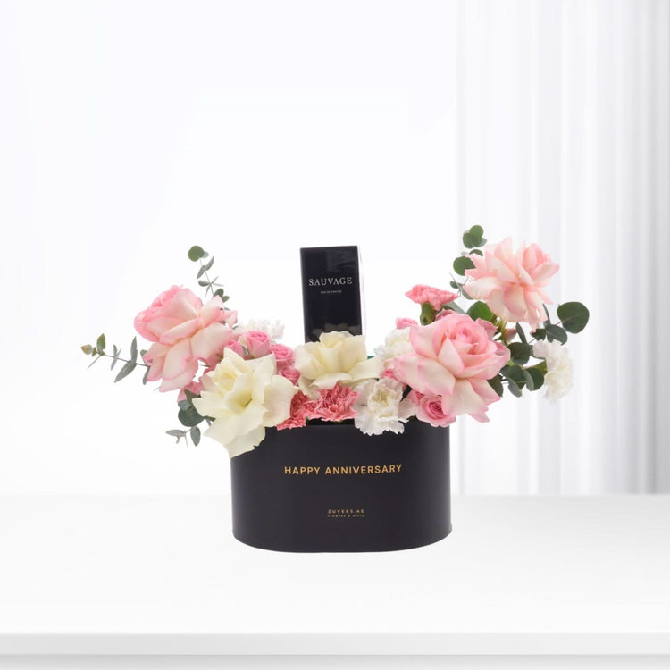 Black box with "Happy Anniversary" holds pink roses, white blooms, and Sauvage perfume.