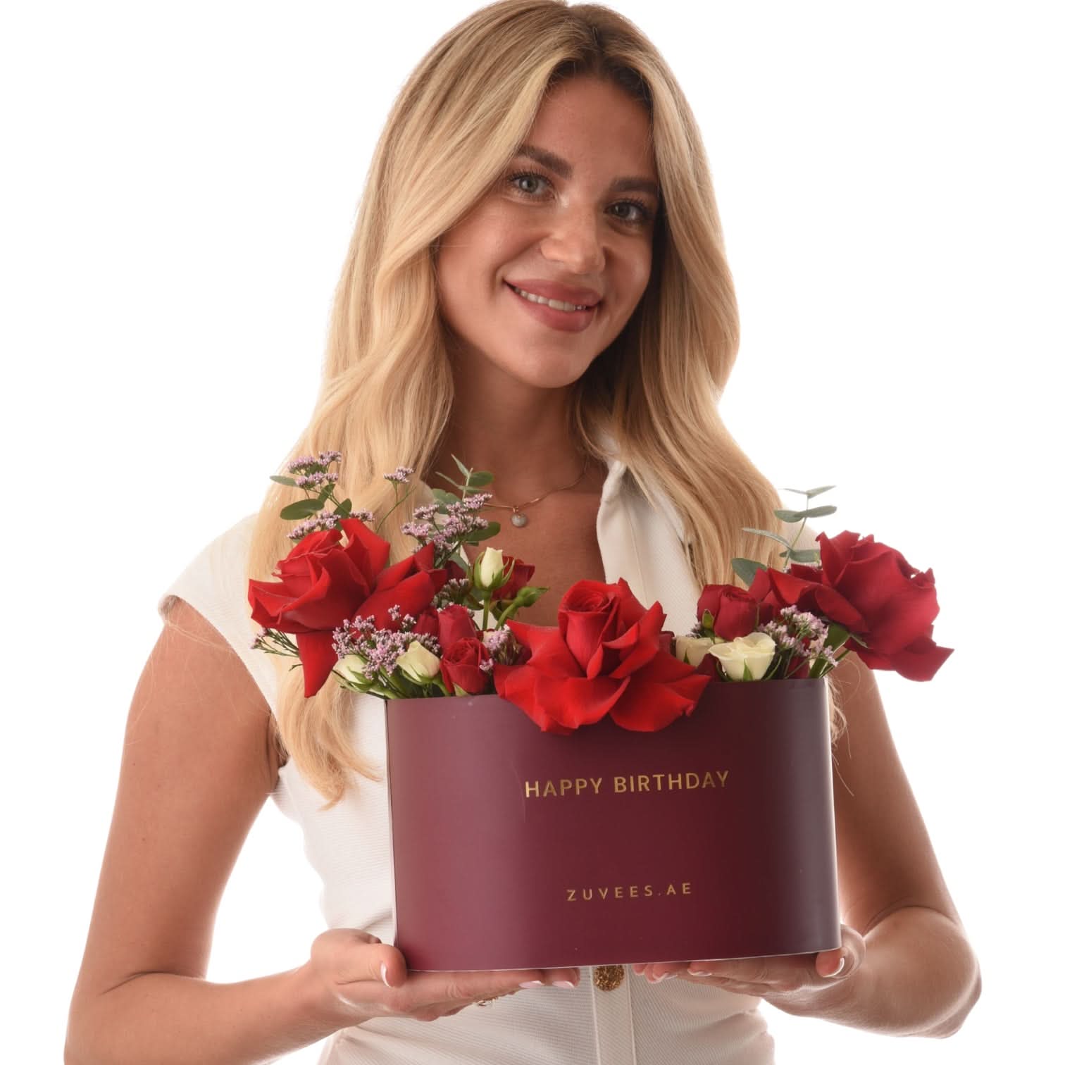 Woman holds burgundy "Happy Birthday" box overflowing with vibrant red roses and white accents.