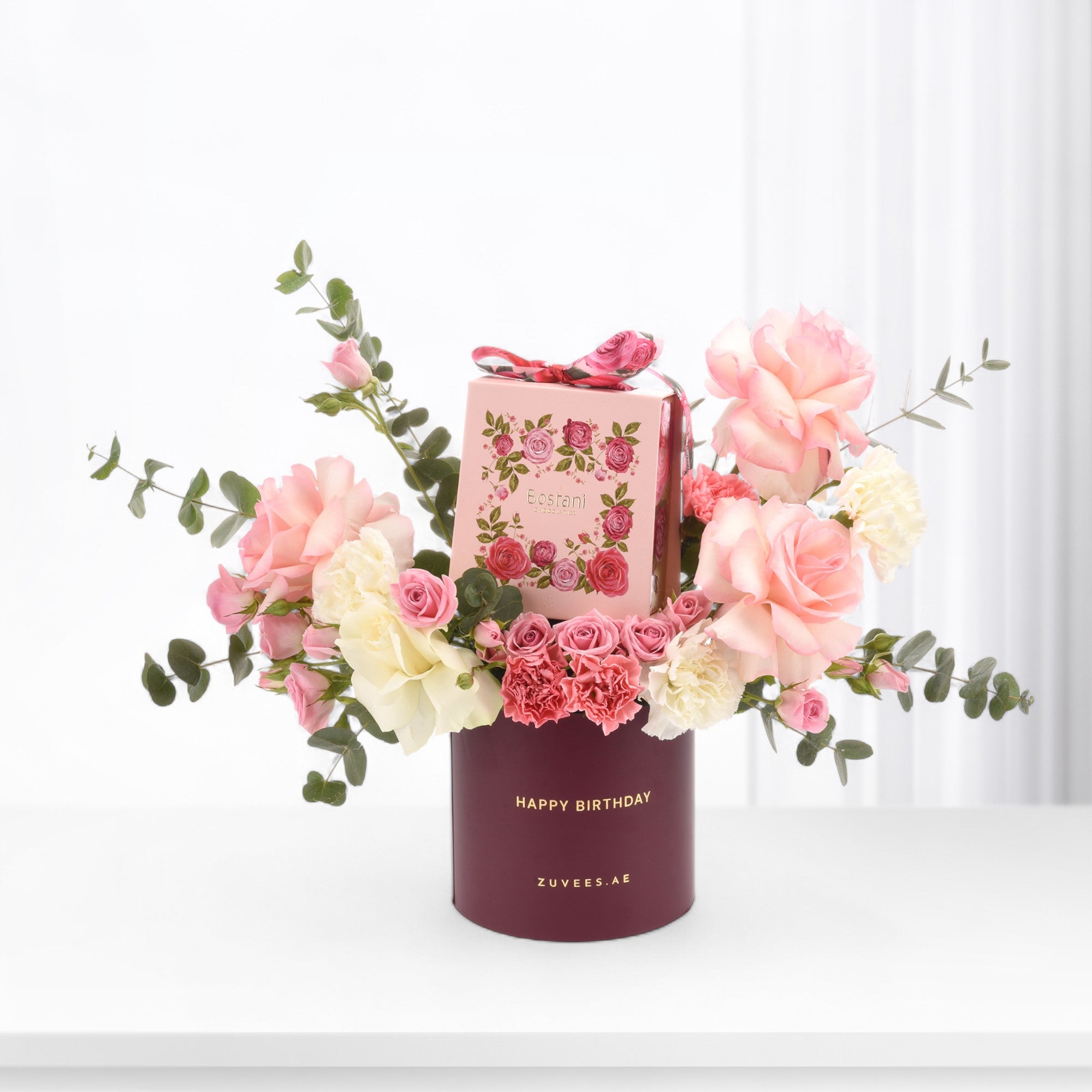 Pink roses and carnations in burgundy birthday box with chocolate gift.