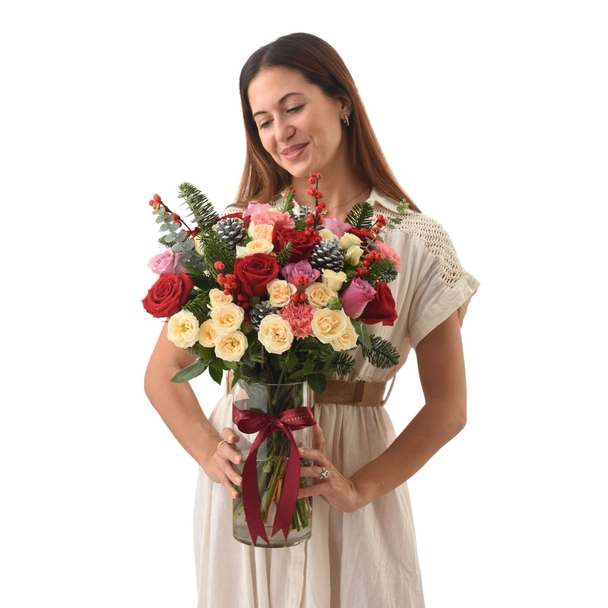 Woman holds festive floral arrangement with red bow, pinecones, and berry accents.