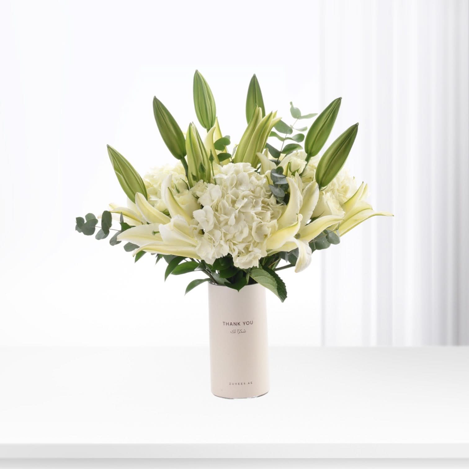 Cream vase with "Thank You" text holds white lilies, hydrangeas, and green buds.