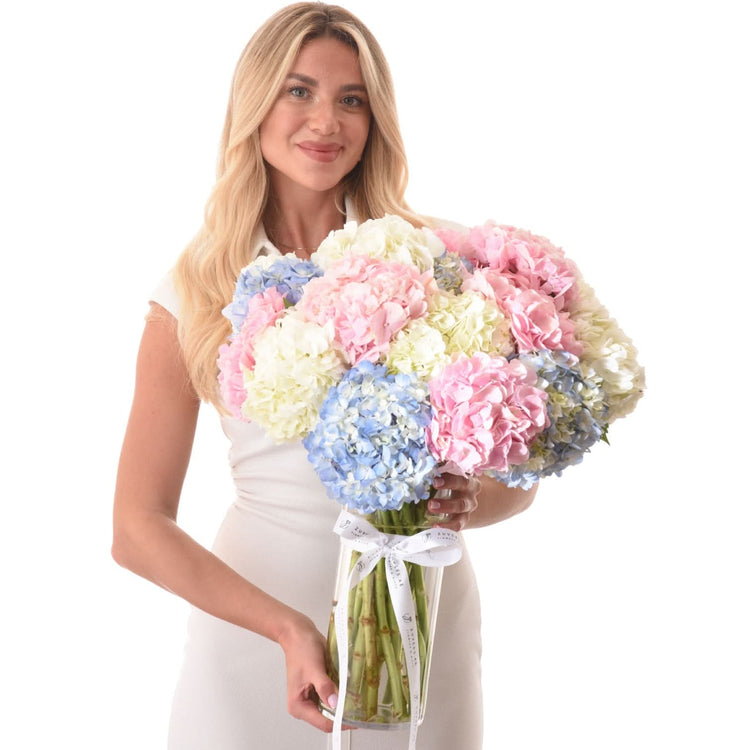 Woman holds pastel hydrangea bouquet in clear vase with white ribbon.