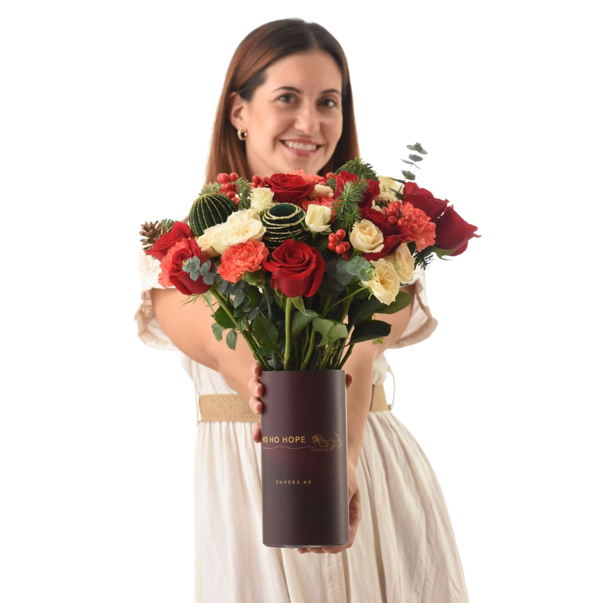 Woman holds festive red, white, and green floral arrangement in branded burgundy tube.