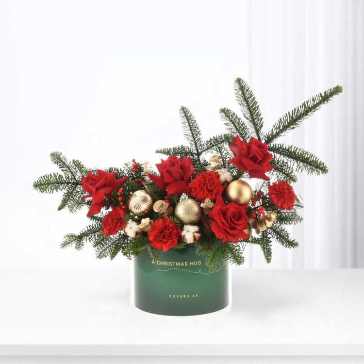 Vibrant red roses, pine, gold ornaments in festive green container.