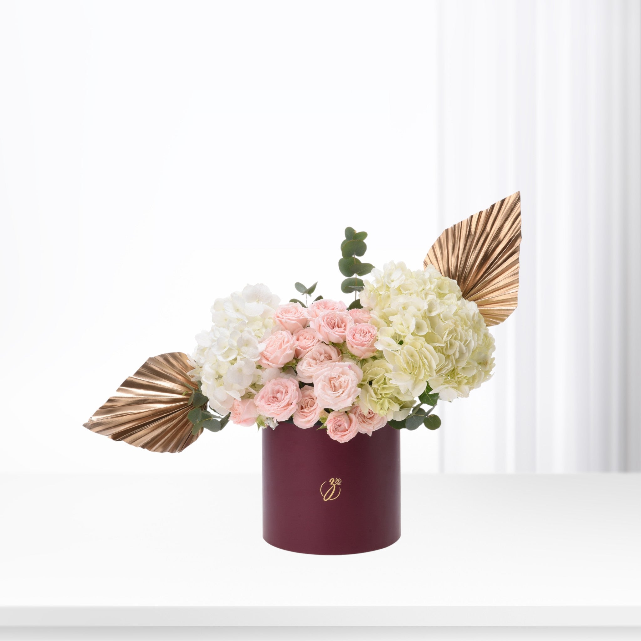 Elegant pink roses, white hydrangeas, gold leaves in burgundy cylinder vase, minimalist luxury floral arrangement.