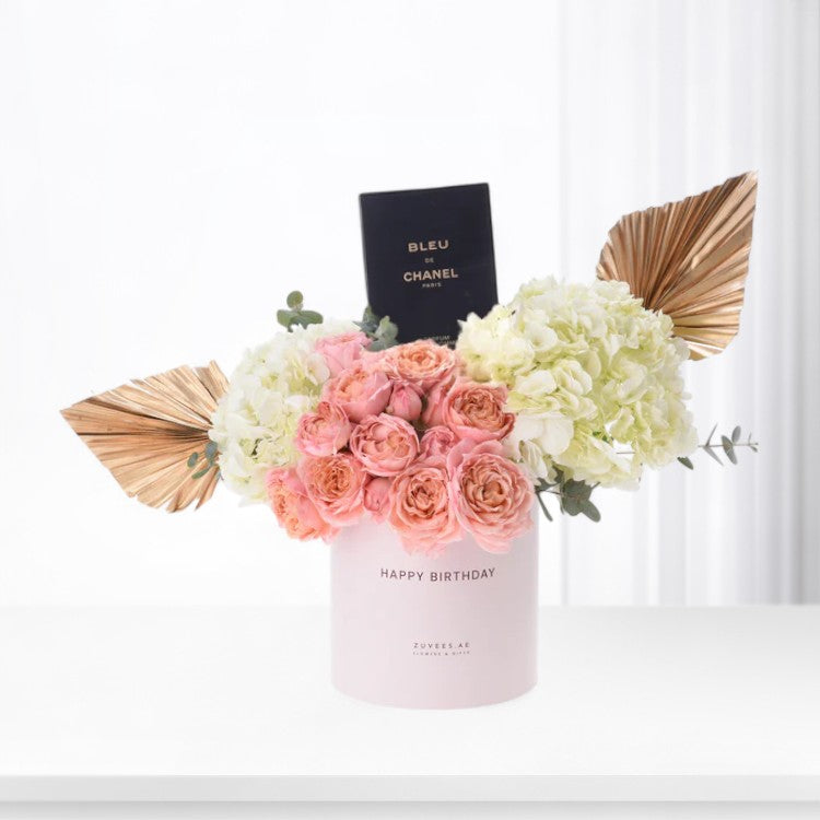 Pink roses, white hydrangeas, gold palm accents, and Chanel perfume in minimalist pink vase.