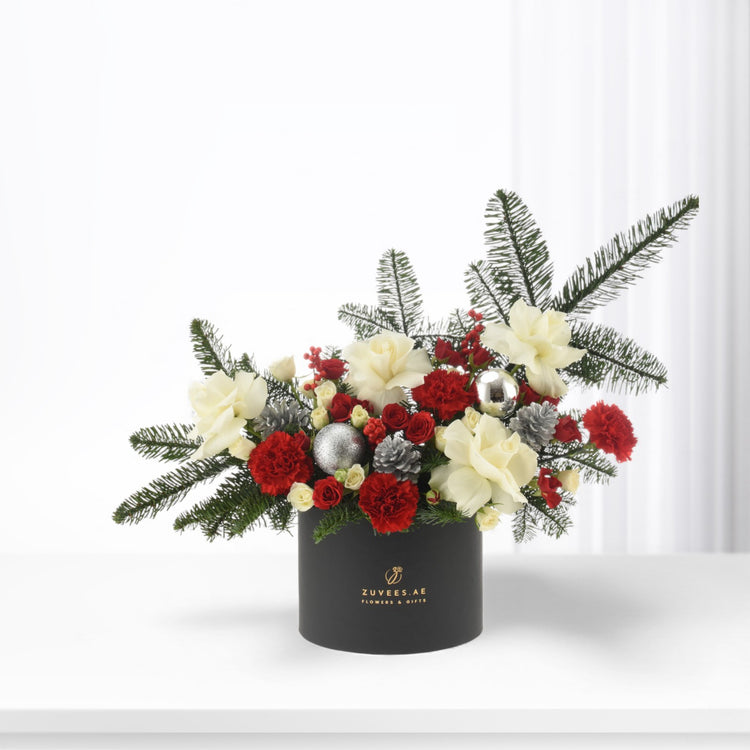 Elegant black box holds festive red and white blooms with pine, silver ornaments, and gold branding.