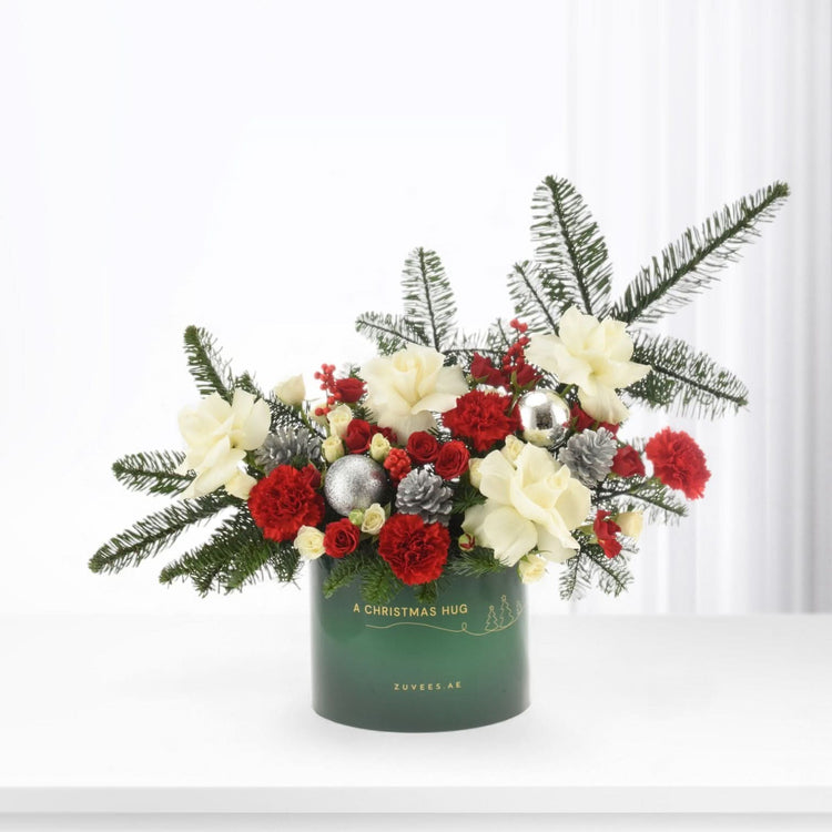Green vase holds red carnations, white roses, pine, and silver ornaments for festive holiday display.