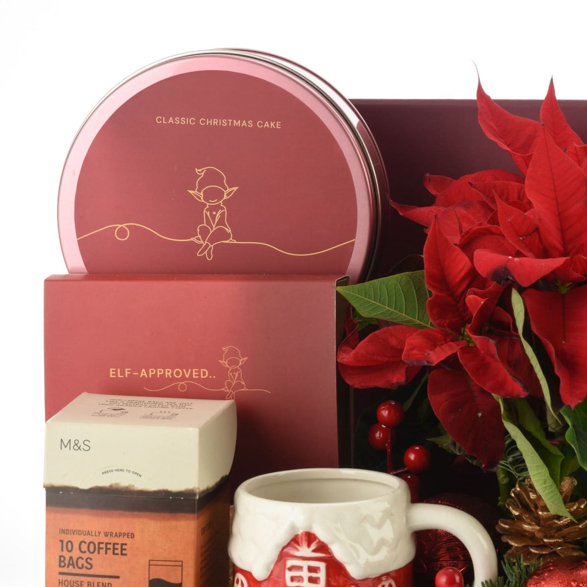 Red tin & mug set with elf-themed Christmas cake and coffee, poinsettias nearby.