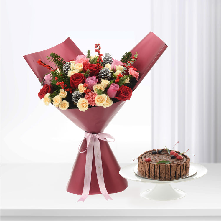 Vibrant red, pink, and cream roses with pinecones and berries, elegantly wrapped in burgundy paper with pink ribbon, beside a chocolate cake.