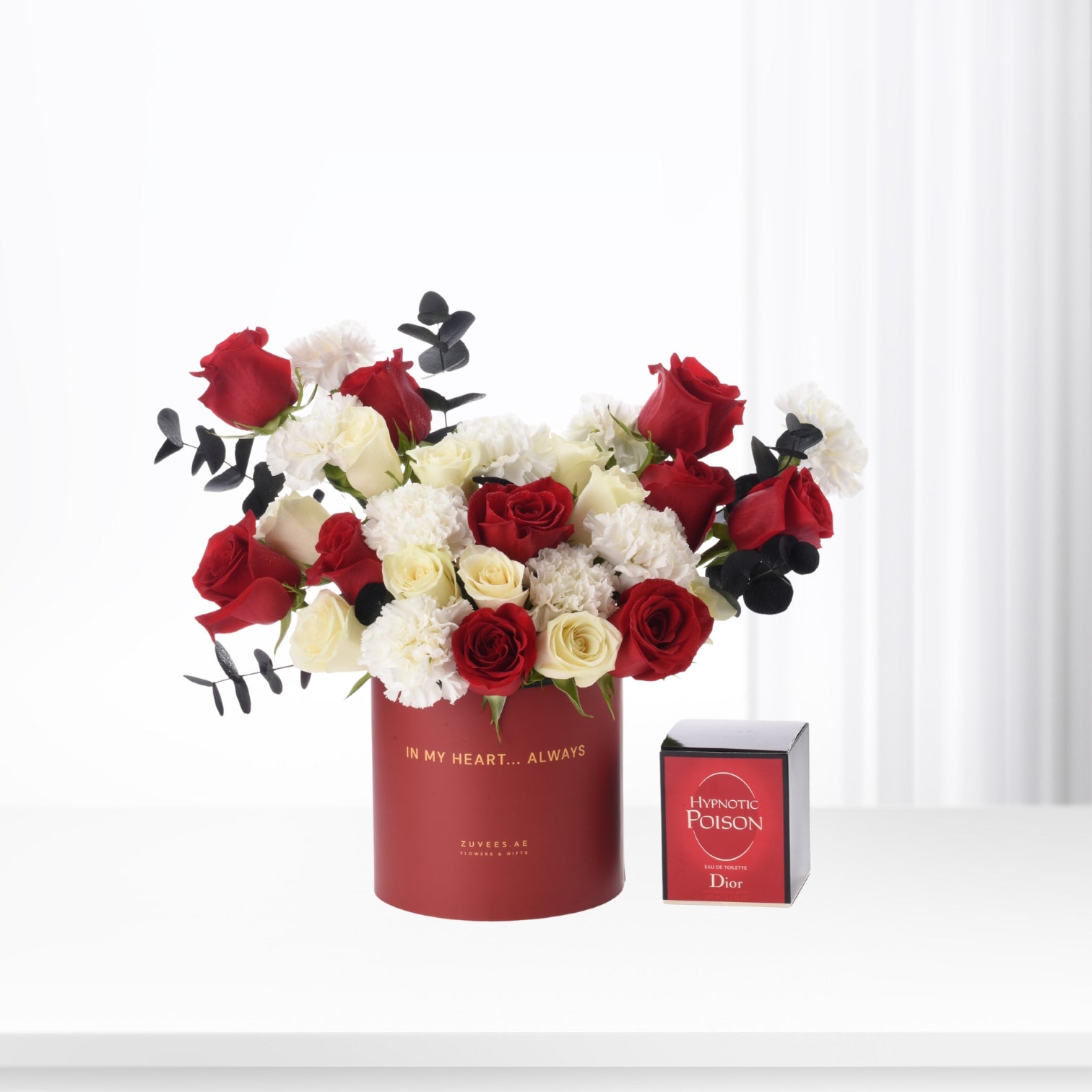 Bold red, white, and black floral arrangement in branded red cylinder beside Dior Hypnotic Poison perfume.