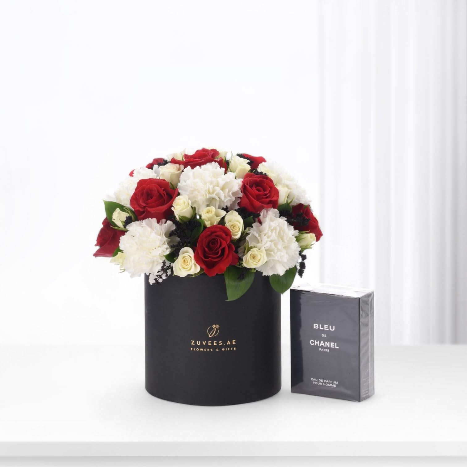 Elegant black box holds red roses and white carnations beside Chanel Bleu perfume.