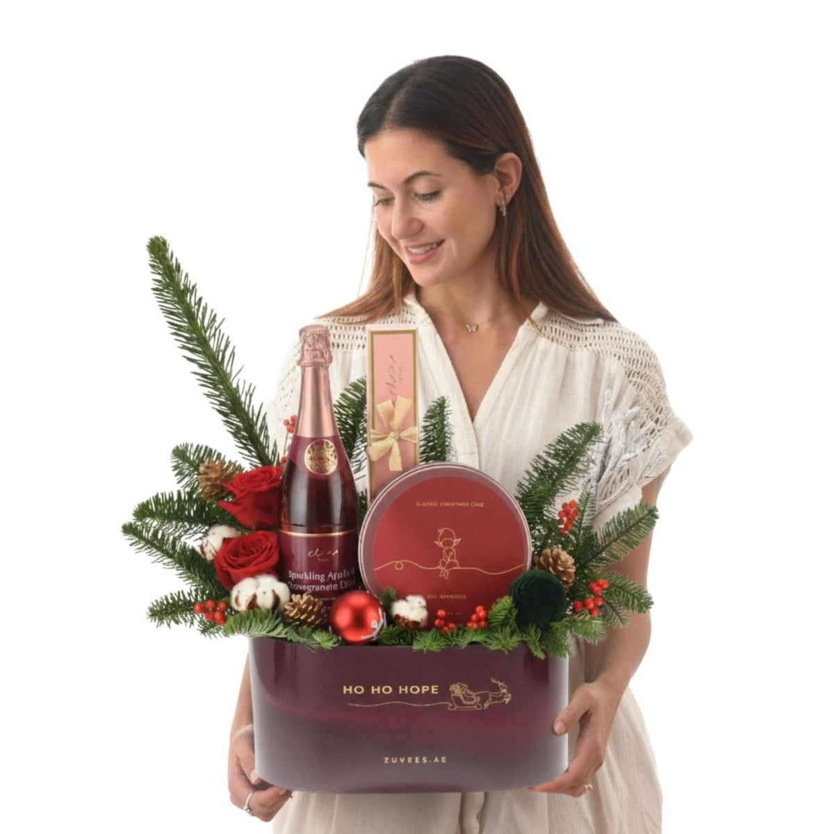 Woman holds festive purple gift basket with champagne, chocolate, pine, and red roses.