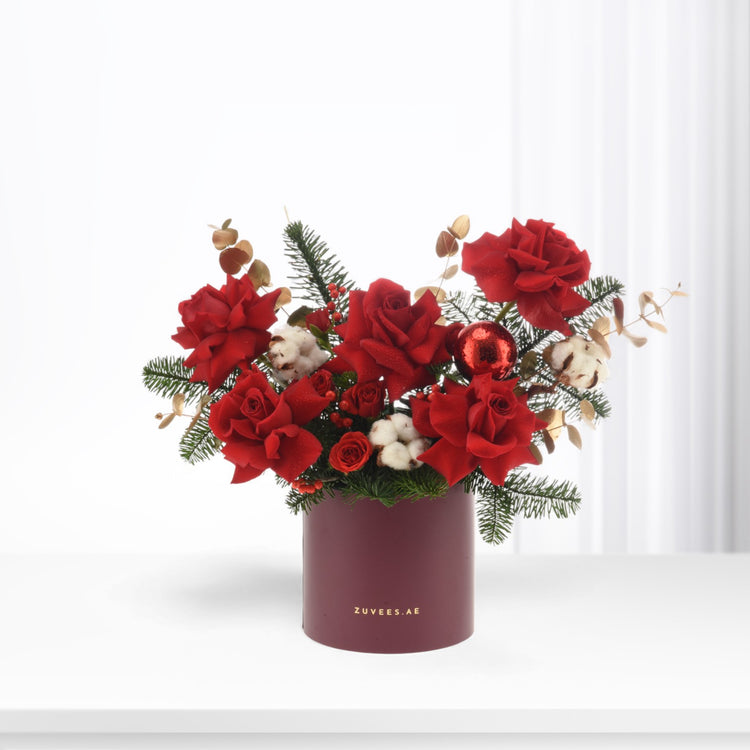 Vibrant red roses, cotton, pine, and berries in burgundy vase.