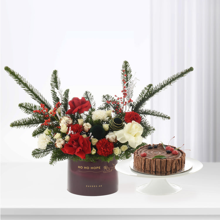 Festive red, white, green floral arrangement with pine, berries, and chocolate Yule log cake.