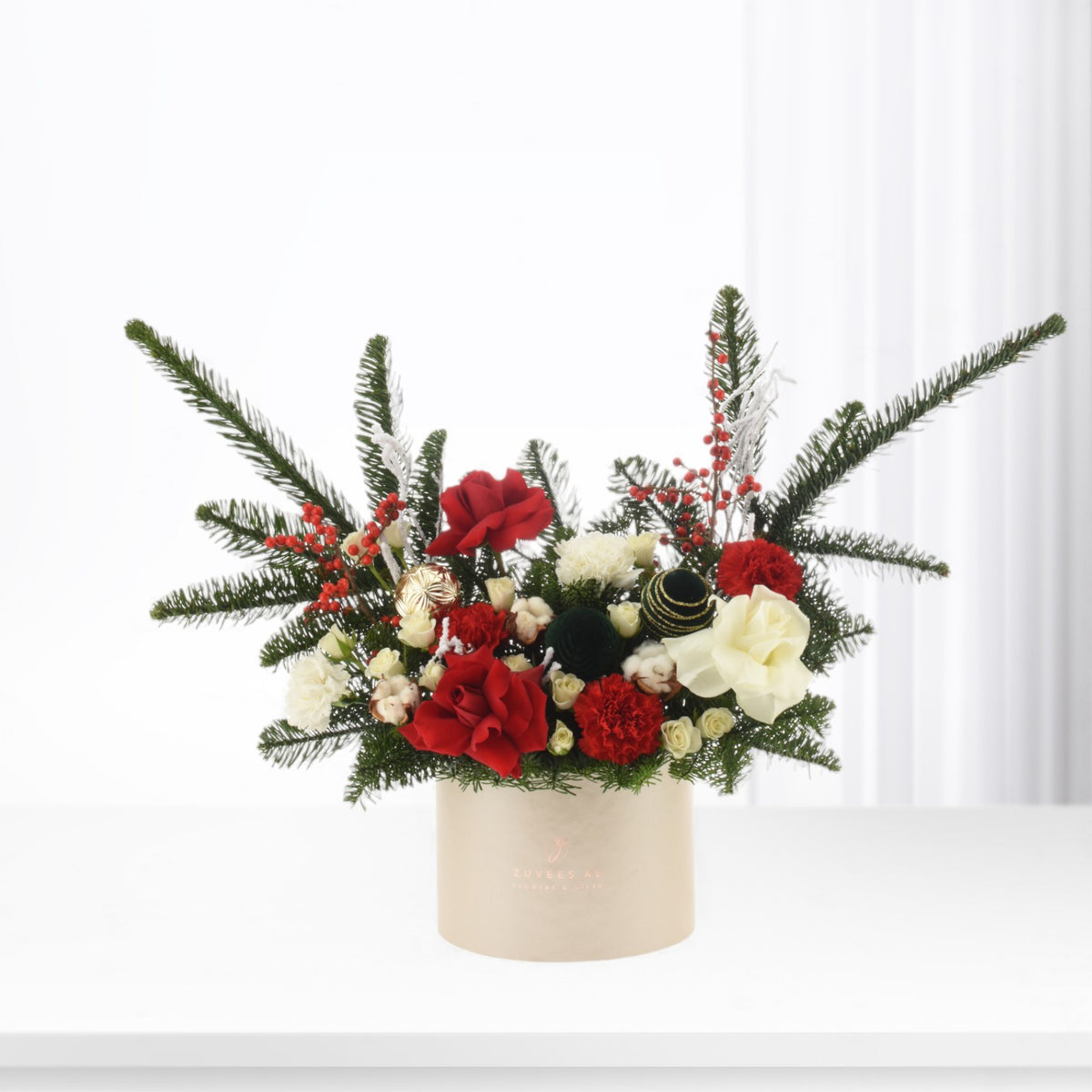 Elegant holiday floral arrangement in cream container with red roses, white blooms, and evergreens.