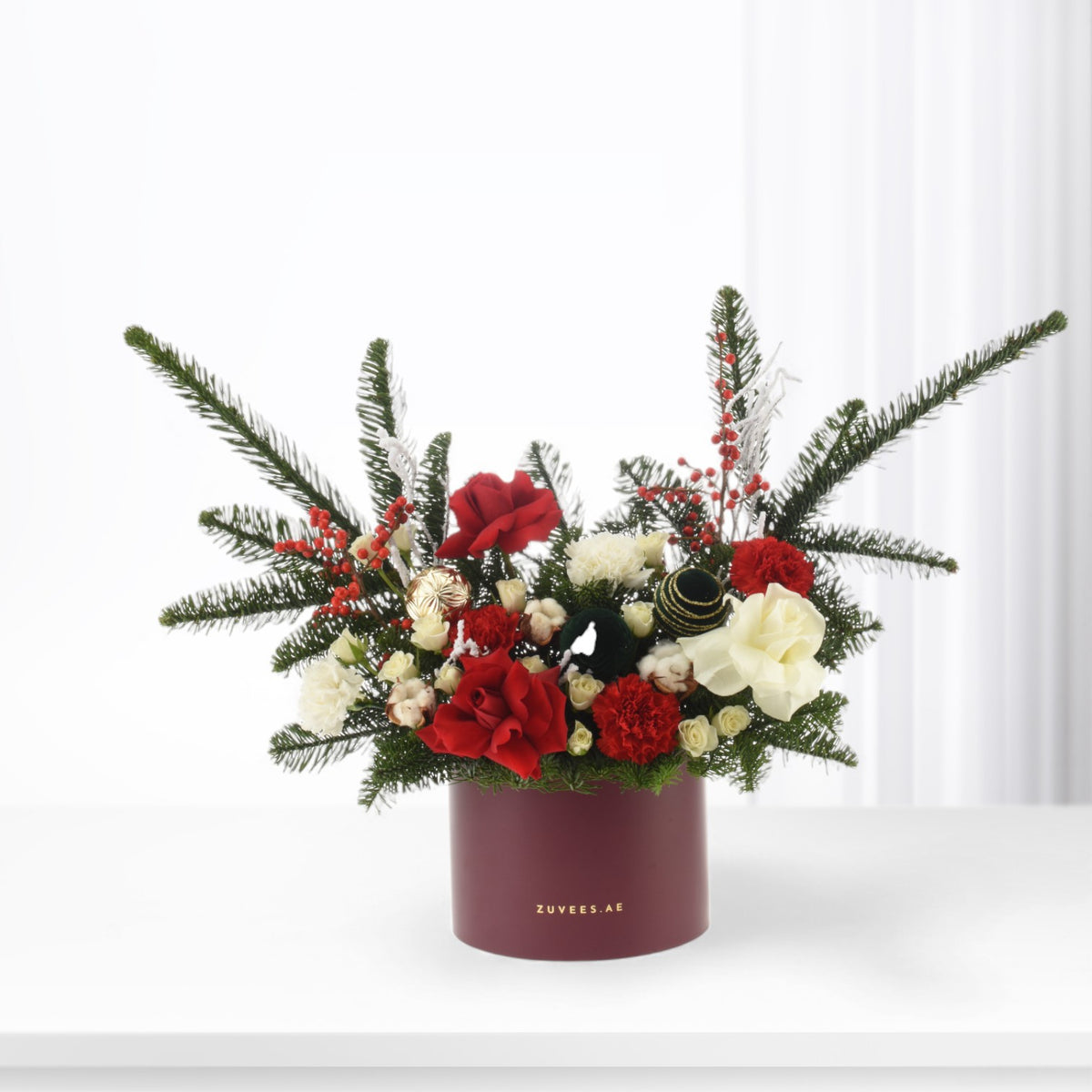 Festive red, white, green floral arrangement with pine, berries, ornaments in burgundy Zuvees box.