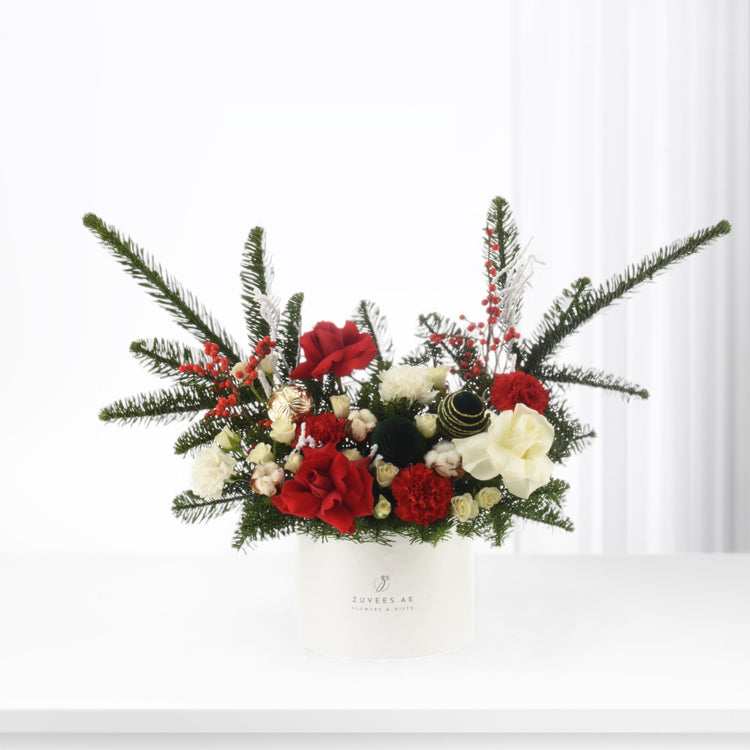 Elegant holiday floral arrangement in white container, red roses, white blooms, pine, berries, gold ornaments.