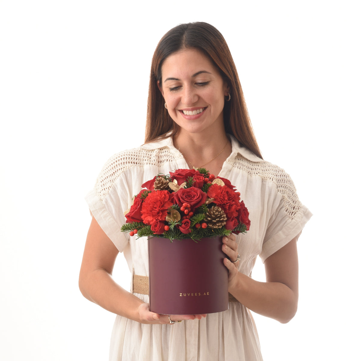Woman holds burgundy box with red roses, carnations, pinecones, and berries.