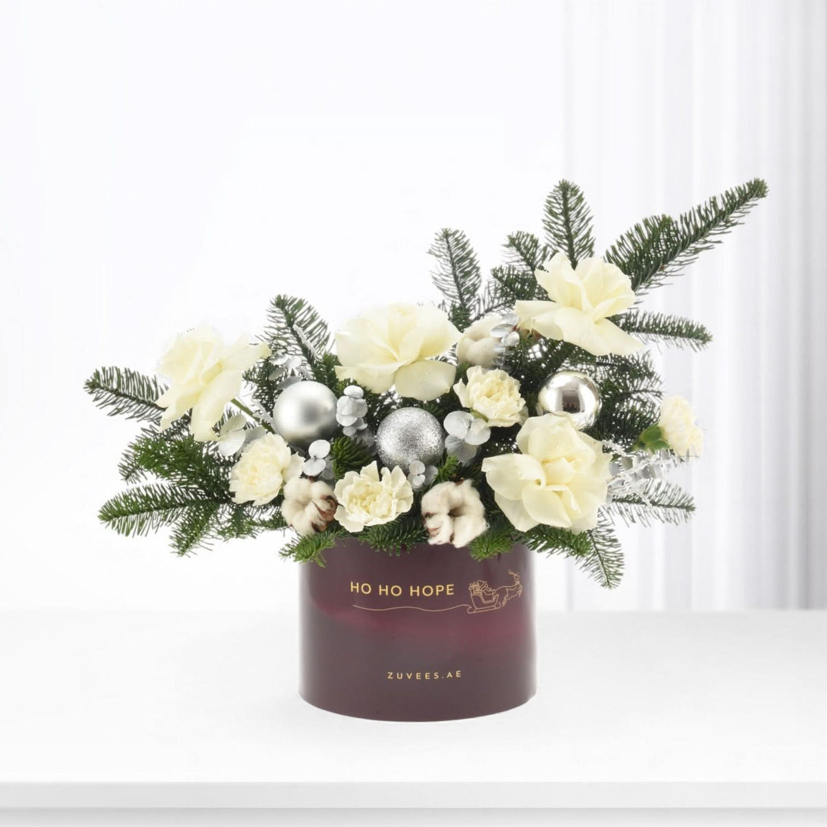 Elegant white floral arrangement with silver ornaments in burgundy holiday box.
