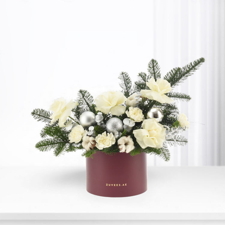 Elegant winter floral arrangement in burgundy box with silver ornaments and white blooms.