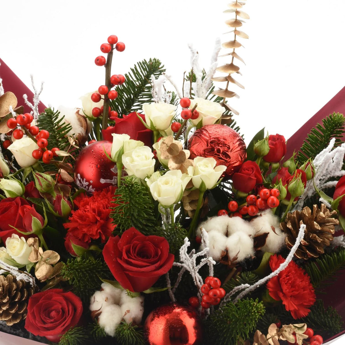 Vibrant red roses, white blooms, holly, pine, and glittering ornaments in festive holiday bouquet.