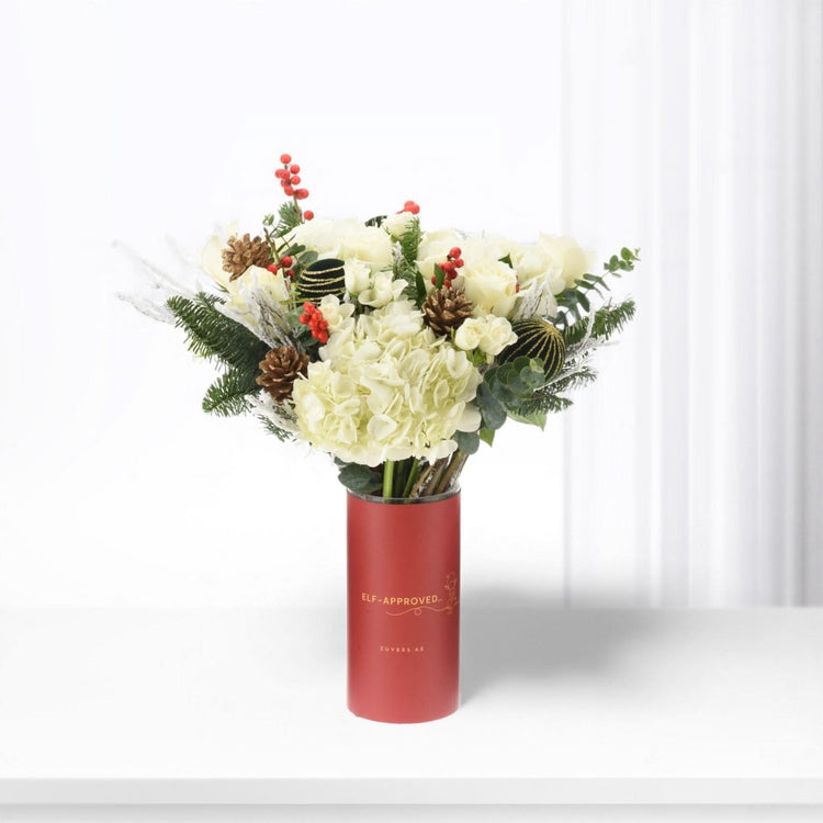 White roses and hydrangeas in festive red vase with pinecones and berries.