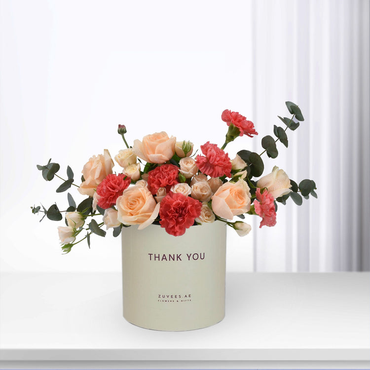 Pastel peach roses and red carnations in cream box with "Thank You" text.