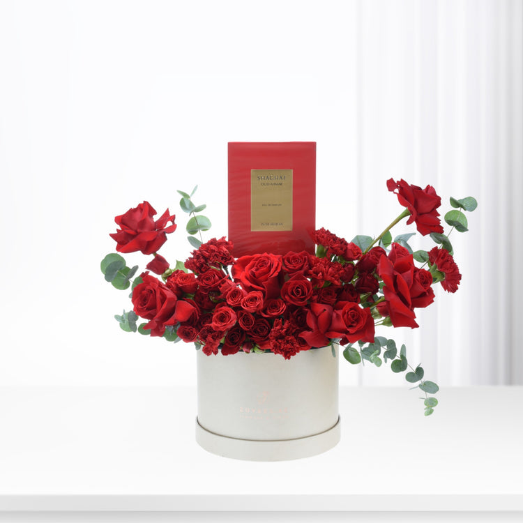 Vibrant red roses and carnations in cream box, accented with eucalyptus and luxury perfume.