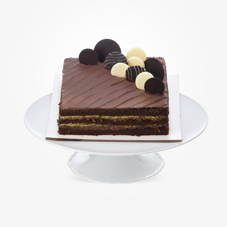 Rich chocolate cake with layered cream, topped with assorted truffles on white pedestal.