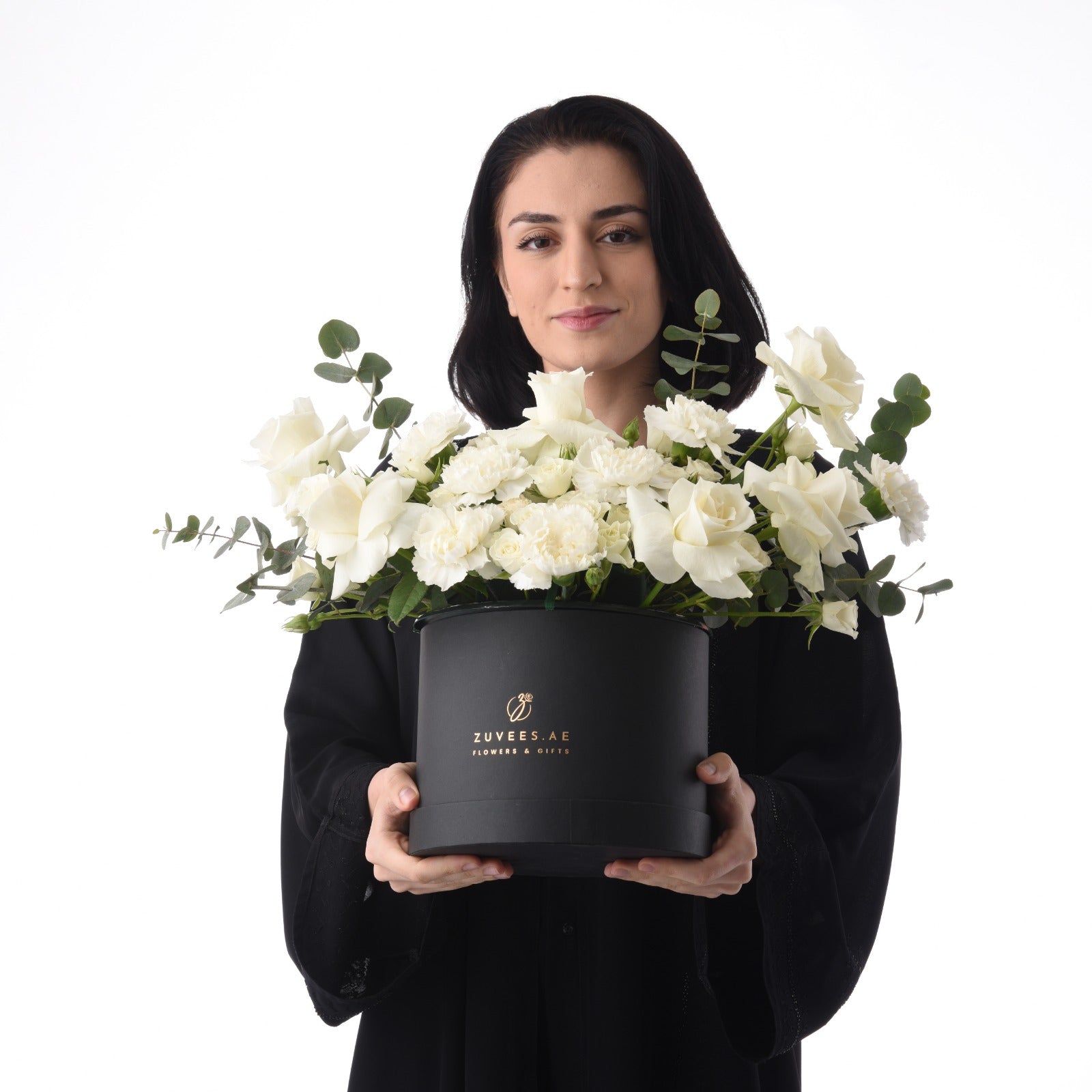Elegant woman holds black box overflowing with pristine white roses and eucalyptus.