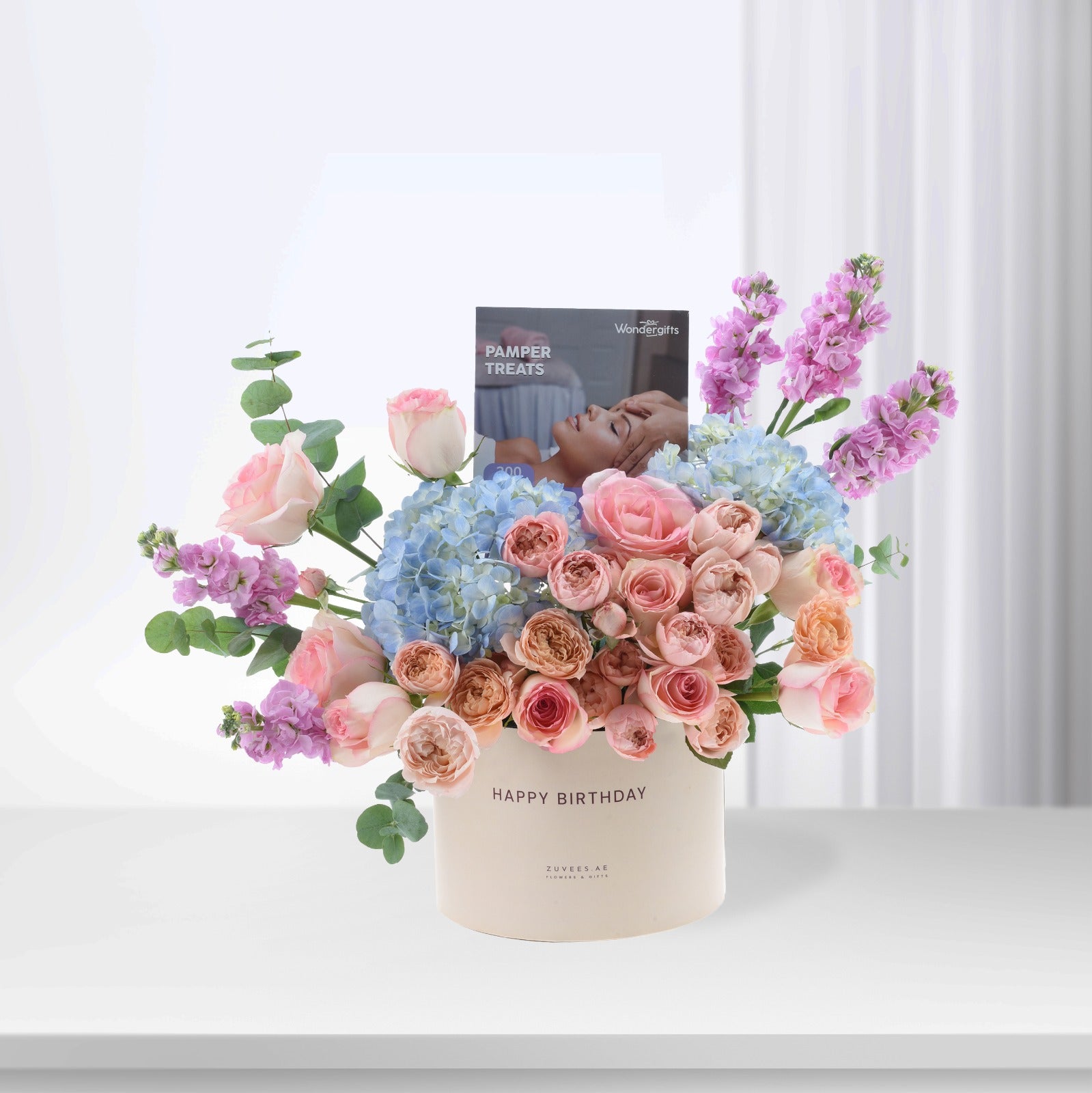 Pastel pink roses, blue hydrangeas, and purple blooms in creamy box with "Happy Birthday" and pamper card.