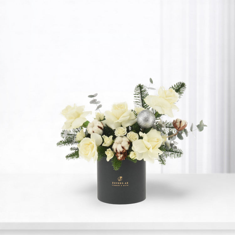 Elegant white rose bouquet in matte black vase with silver ornament and greenery.