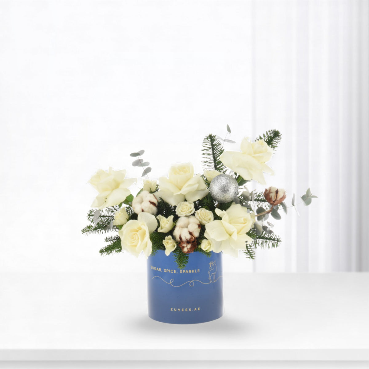 White roses, cotton, and evergreens in blue vase with silver ornament.
