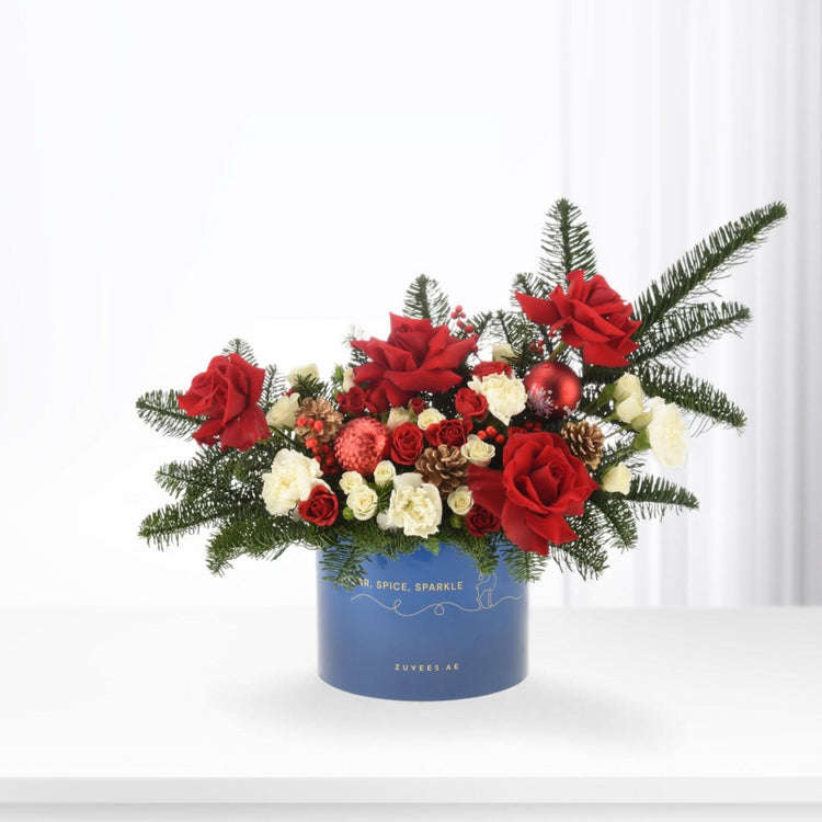 Vibrant red roses, white blooms, pine, and ornaments in festive blue box.