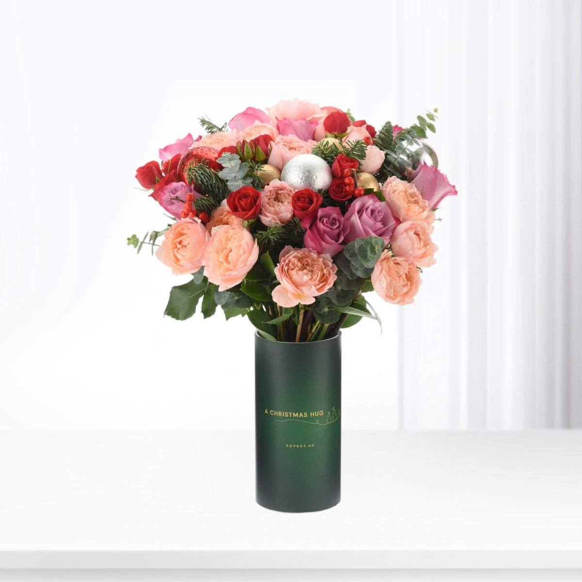 Vibrant pink, red roses and berries in festive green vase.
