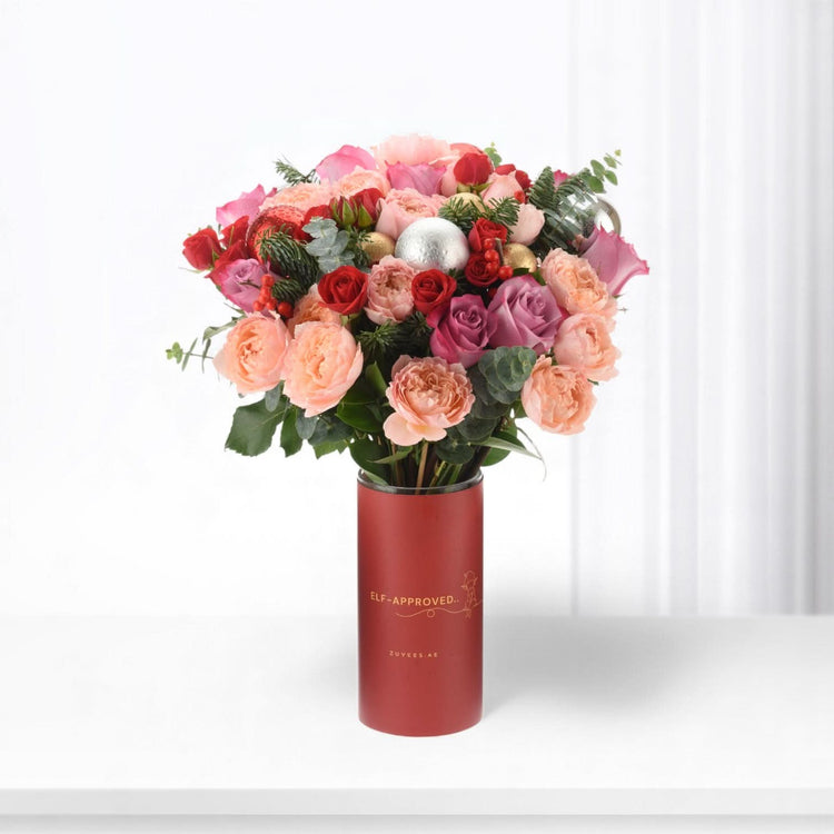 Vibrant red, pink, and gold roses in festive red cylinder vase with "Elf-Approved" text.