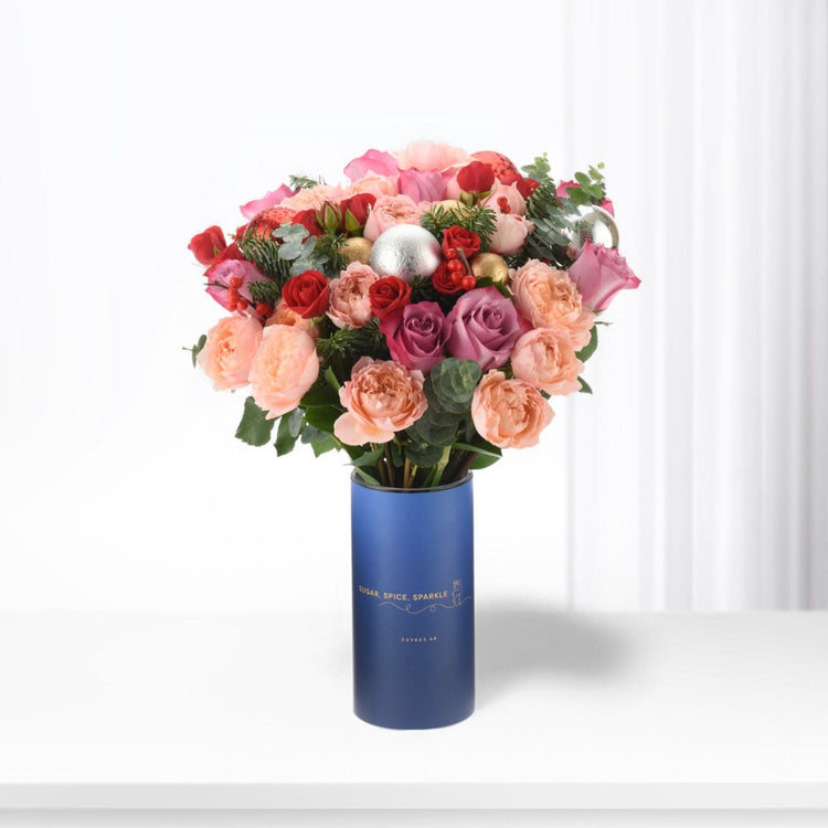 Vibrant pink, red, and purple roses in festive blue cylinder vase with gold accents.
