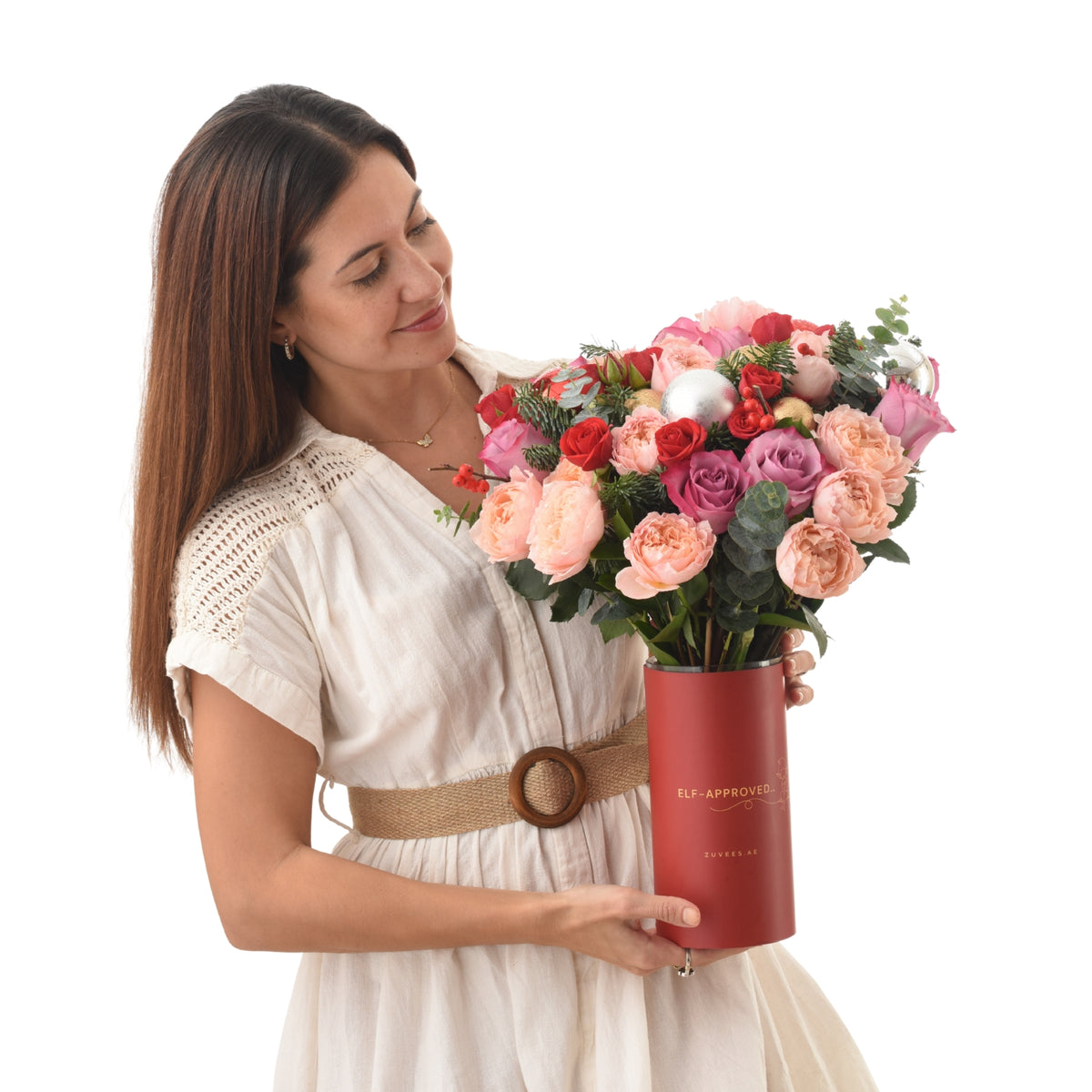Woman holds festive red cylinder bouquet with roses, berries, and silver ornaments.