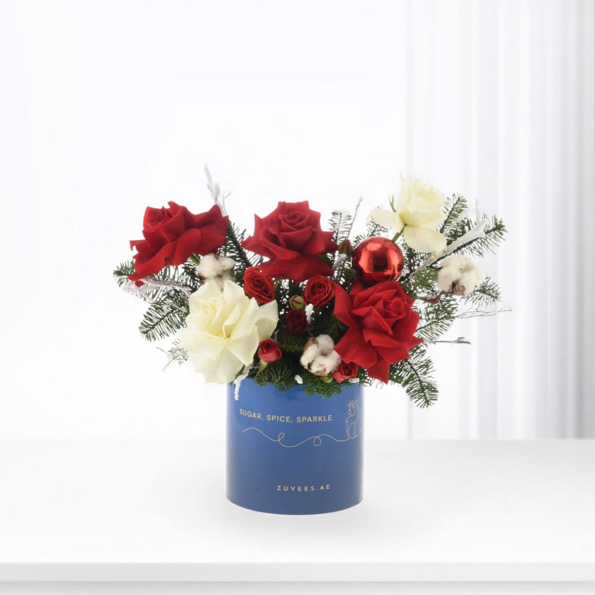 Vibrant red and white roses with pine, cotton, red ornament in blue "Sugar, Spice, Sparkle" vase.